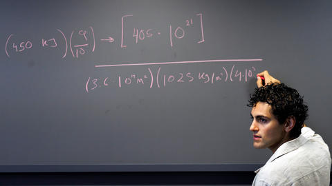 A student writes a math equation on a chalkboard