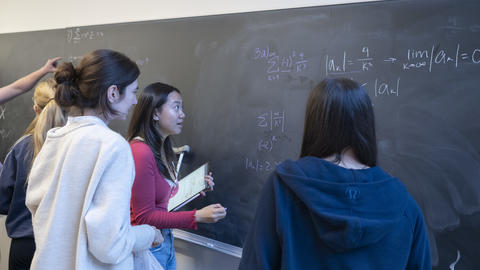 Students look at a math equation on a chalkboard