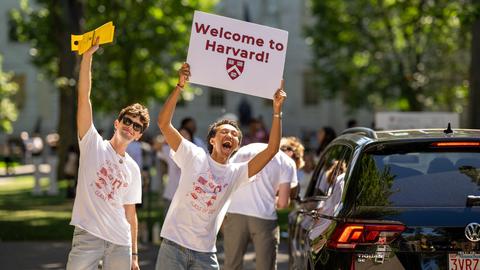 Two students waving in and welcoming first-year families driving into the Yard during first-year move-in.