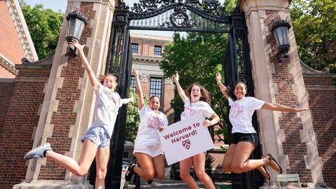 Students jump with excitement in front of a Harvard gate.