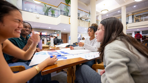 Four students sitting around the table laughing the night before Housing Day making a poster for the Yard storm.