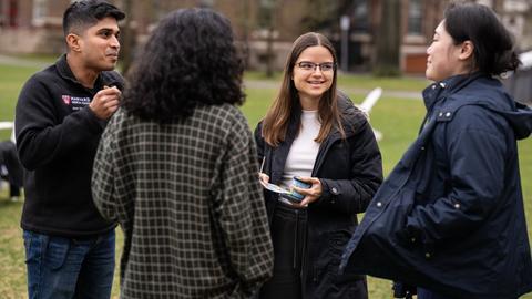 Four students gathered in the Radcliffe Quad lawn eating and talking.