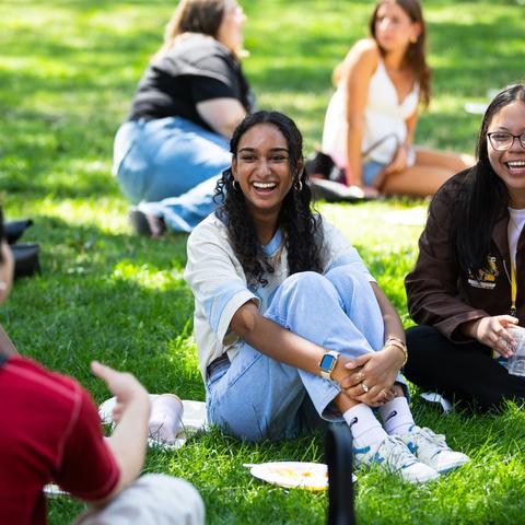 Students sitting on the Harvard Yard lawn laughing during their first-year pre-orientation program.