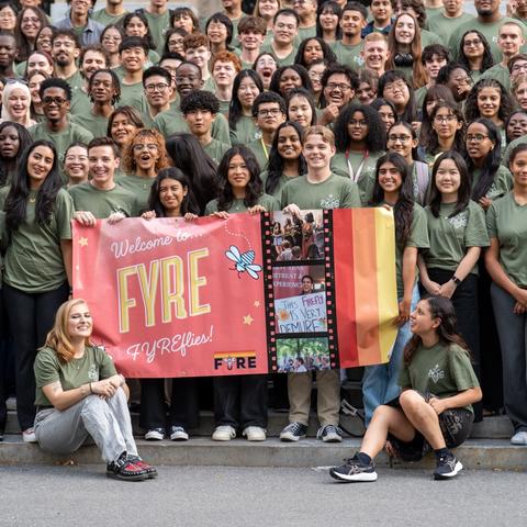 A group shot of students during their First-Year Retreat Experience pre-orientation program on Widener steps holding a FYRE banner.