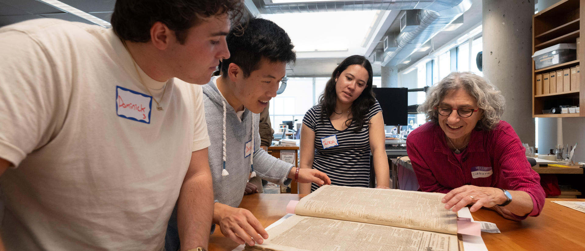 Students look at an old book while an instructor points out text.