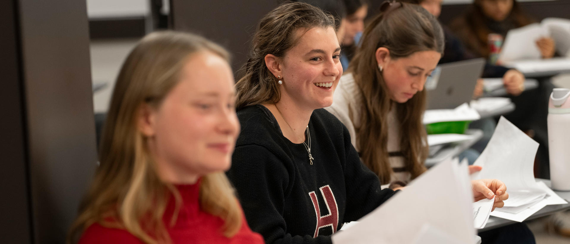 A student smiles in class while holding a paper.
